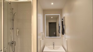 Un baño moderno con ducha de vidrio, lavamanos blanco y espejo con marco iluminado.