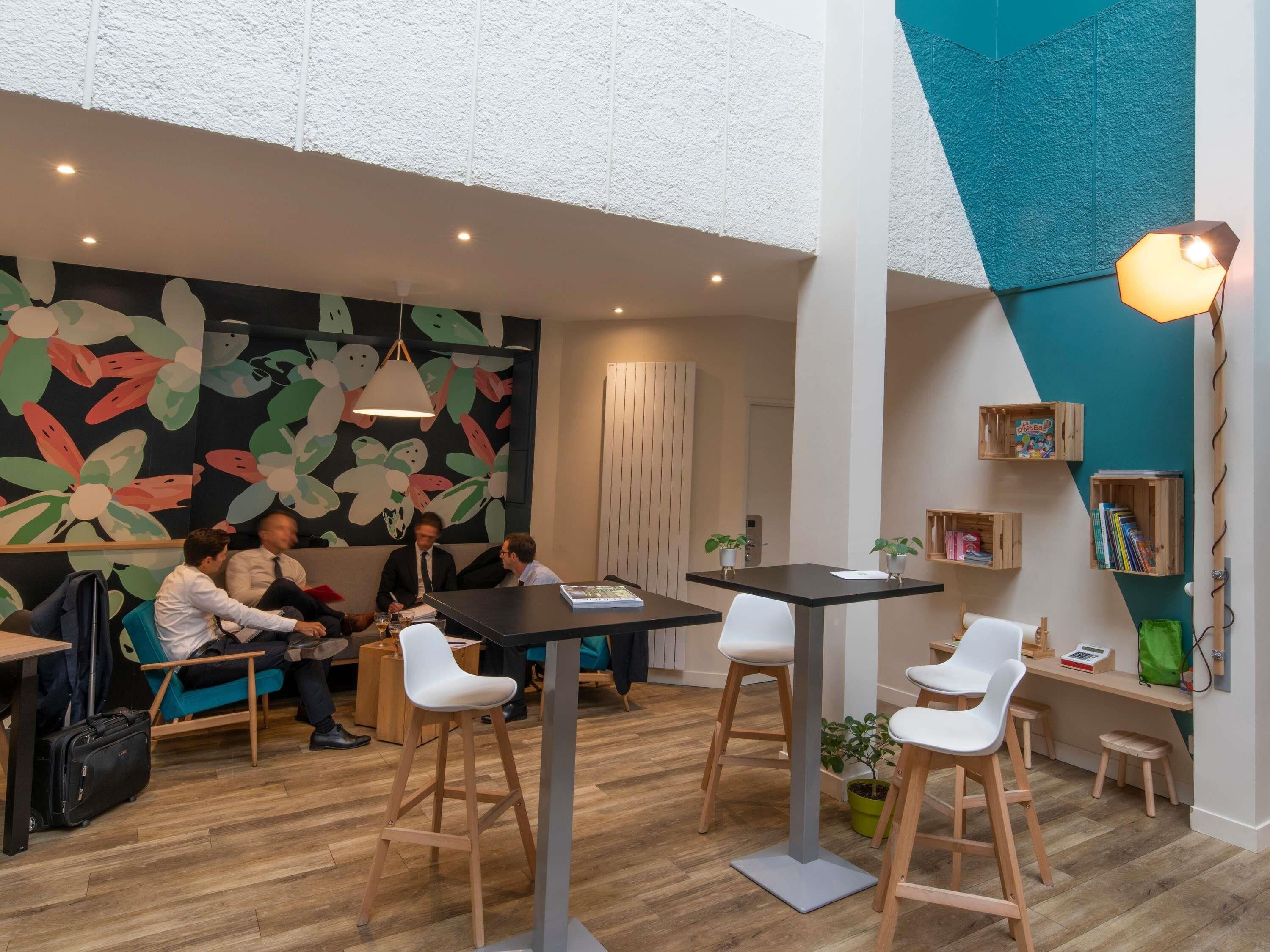 A modern meeting room with wooden flooring, white chairs, a black table, and a colorful abstract wall.
