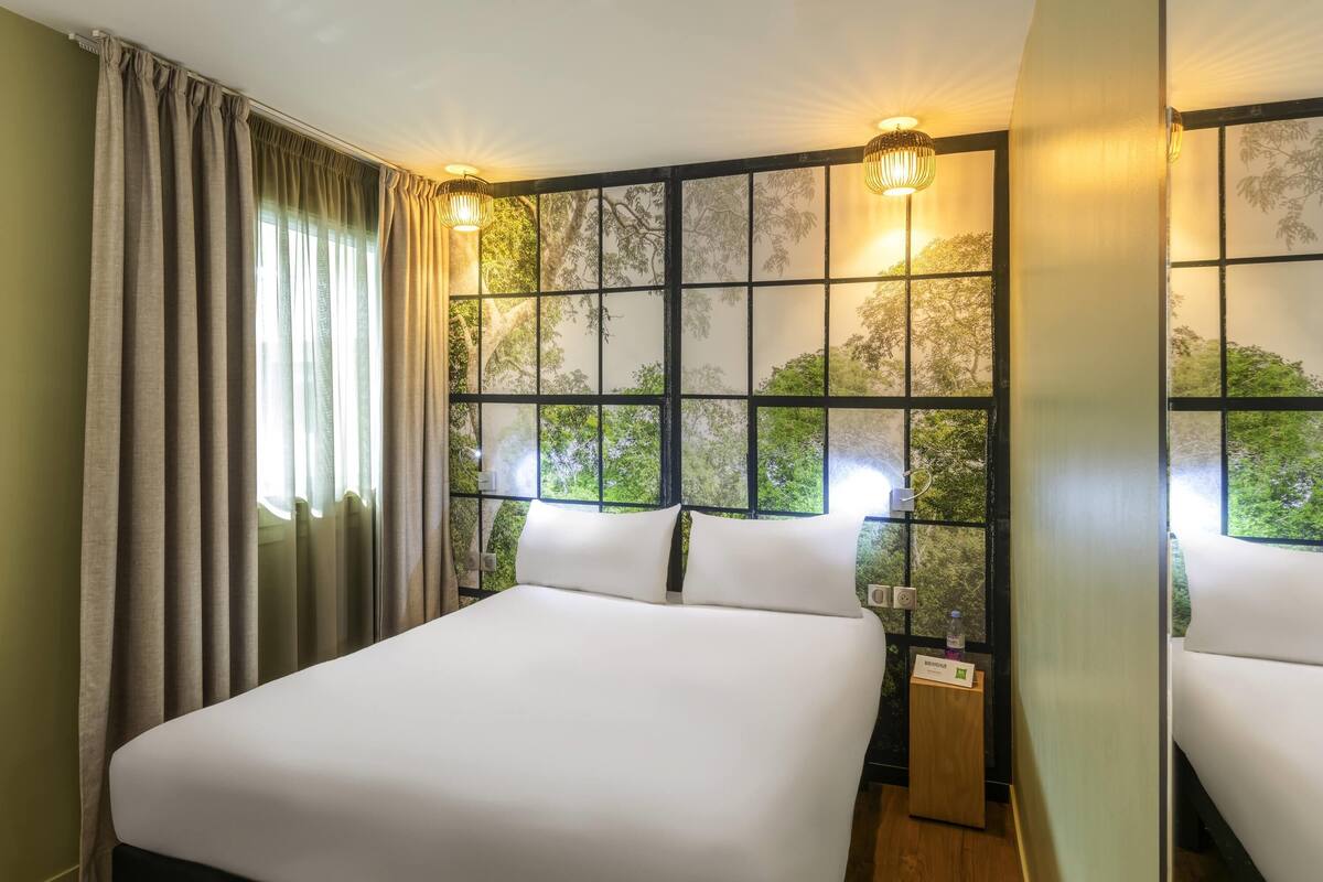 A hotel room with a large bed, a nightstand, a lamp, and a window with a view of trees.
