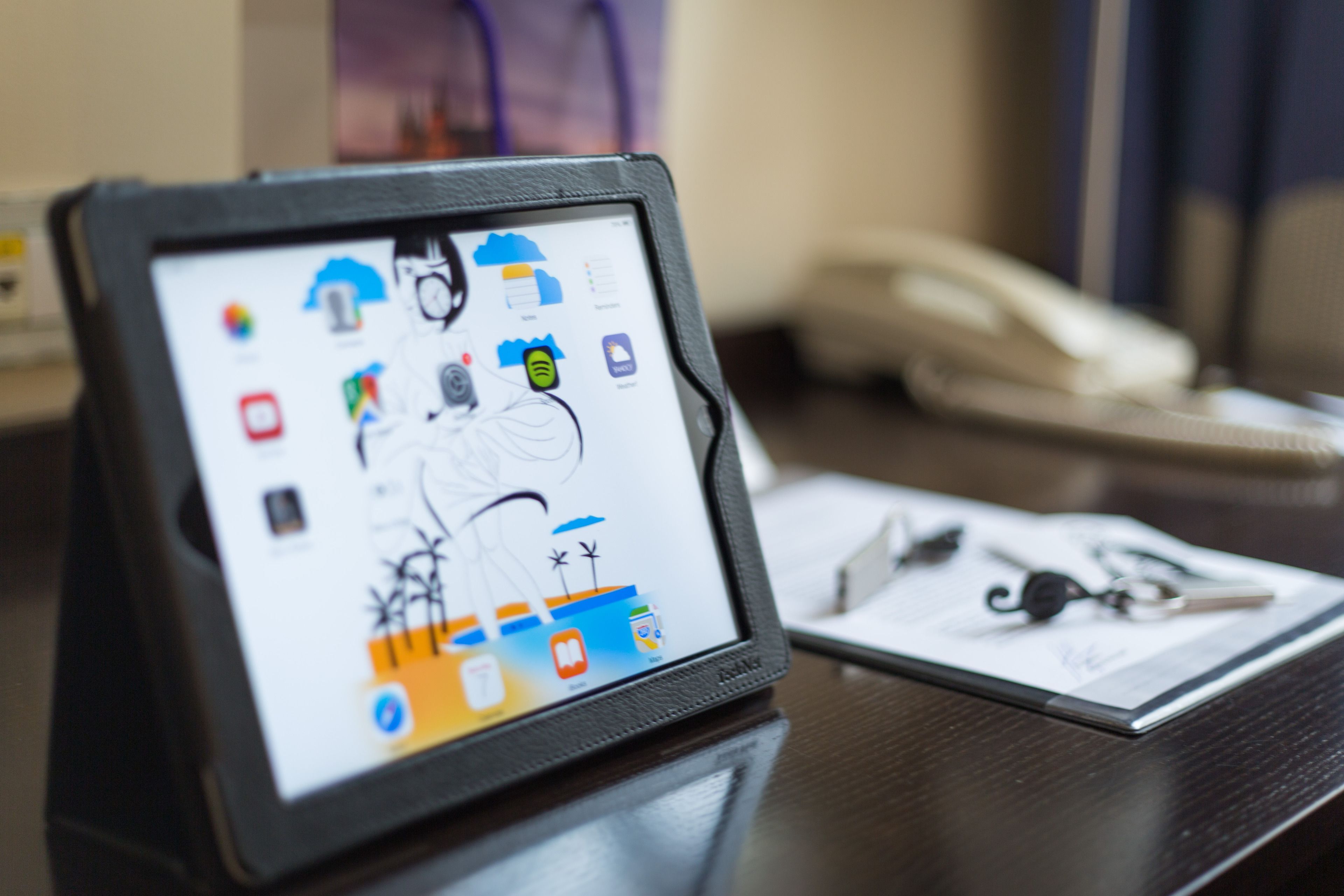 Una tableta mostrando varios iconos de aplicaciones sobre un escritorio con un teléfono y llaves.