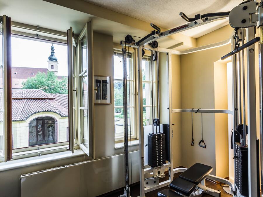 Un gimnasio con equipo de ejercicio, ventanas amplias y vistas a un edificio con torre.