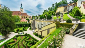 A formal garden with geometric hedges, a central fountain, and a staircase leading to a building with a tower. - Aria Hotel Prague (Prague)