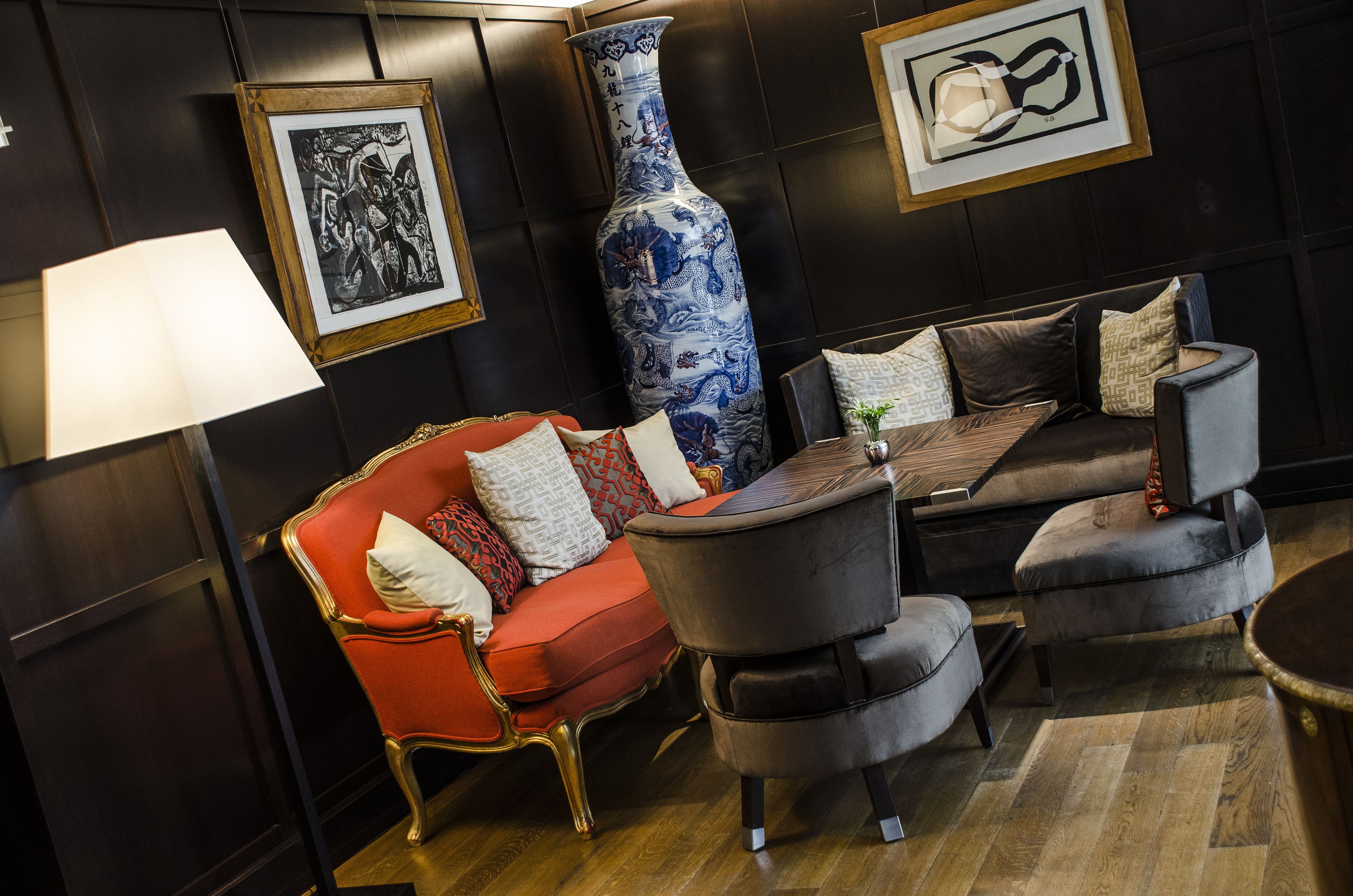 Une pièce avec un canapé rouge, un fauteuil gris, une table basse en bois et un grand vase bleu.