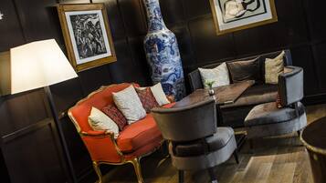 Une pièce avec un canapé rouge, un fauteuil gris, une table basse en bois et un grand vase bleu.