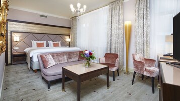 Una habitación de hotel con cama, sofá, sillones, una mesa de centro y televisión.