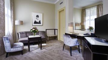 Habitación de hotel con sofá, dos sillones, escritorio, televisor y un cuadro en la pared.
