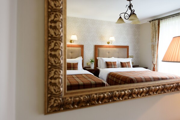 Quarto de hotel com duas camas, um espelho grande e um candelabro.