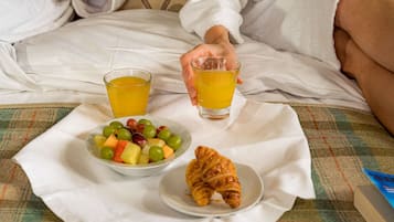 Un desayuno con un bol de fruta, dos vasos de zumo de naranja y un croissant sobre una cama.