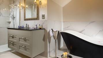 A modern bathroom with a marble floor, a freestanding bathtub, a vanity with drawers, a large mirror, and a chandelier.