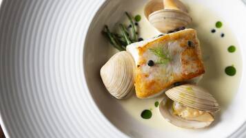 A white plate with a piece of fish, clams, and green garnish.
