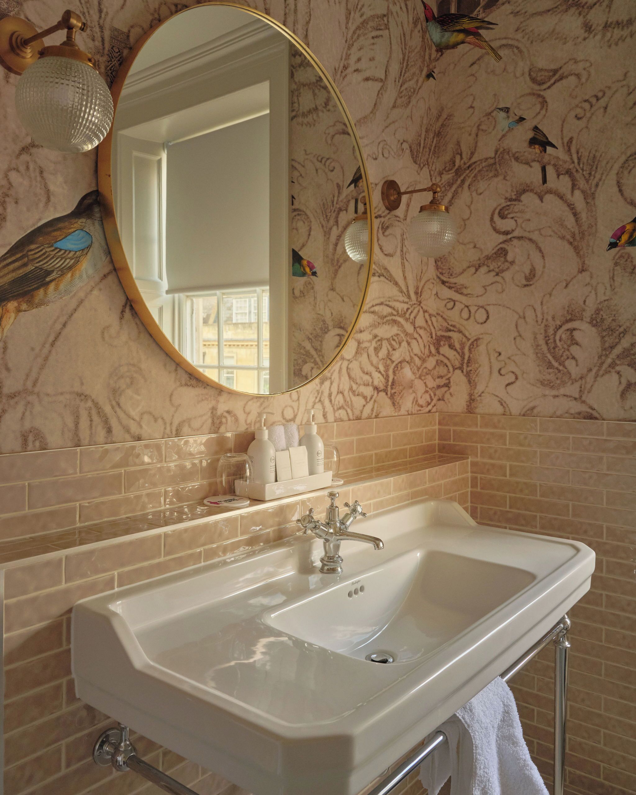 A bathroom with a white sink, a gold-framed mirror, and a decorative wall with floral patterns.