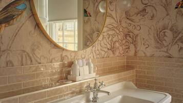 A bathroom with a white sink, a gold-framed mirror, and a decorative wall with floral patterns.