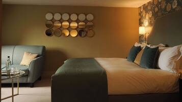 A hotel room with a bed, a sofa, a small table with a bottle and glasses, and a wall-mounted mirror arrangement.