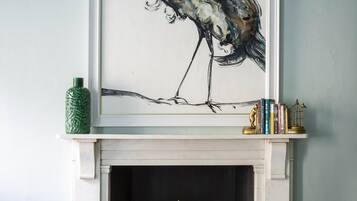 A framed artwork of a bird on a mantelpiece above a fireplace with decorative items below.