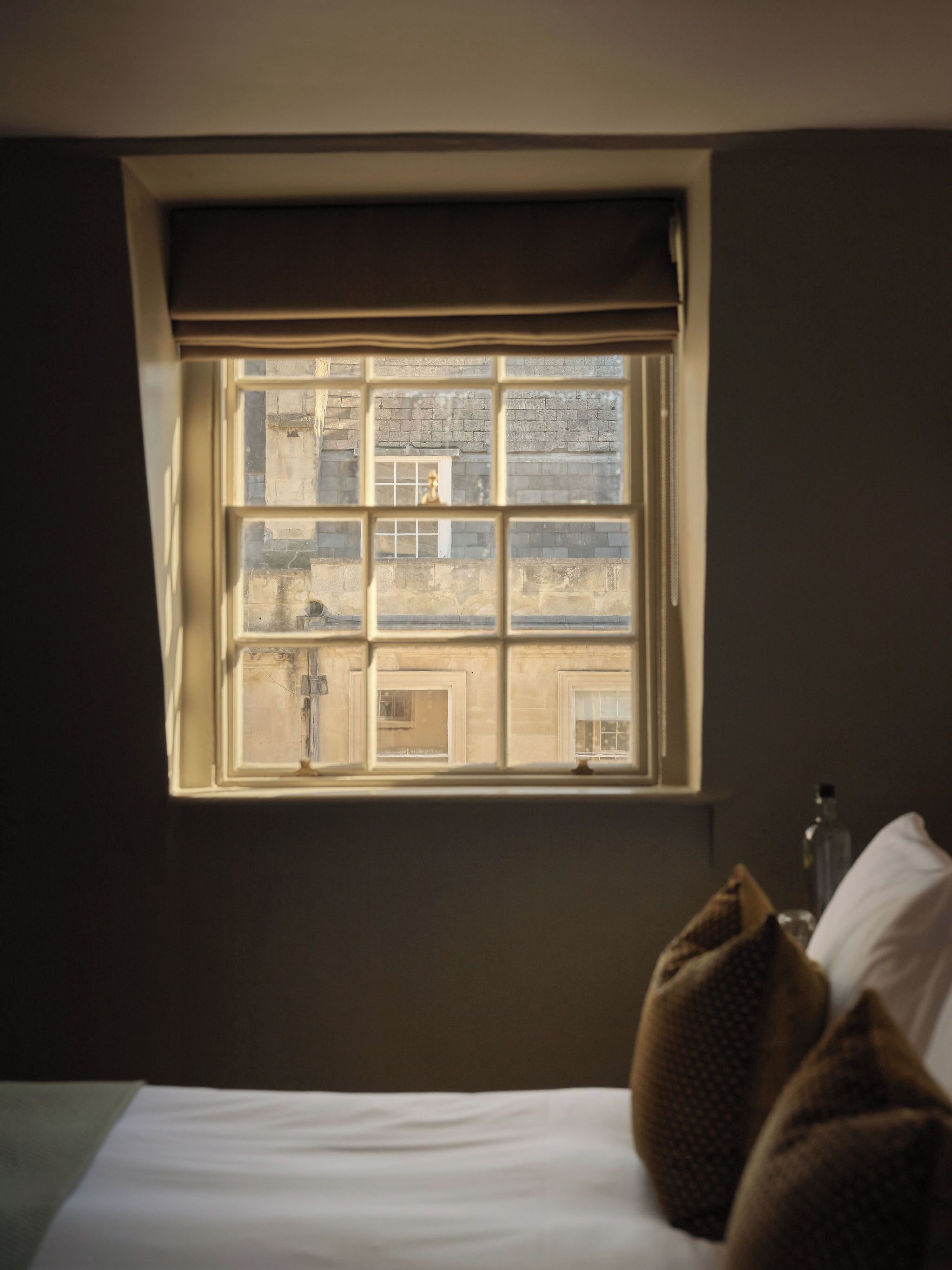 Une chambre avec une fenêtre, un lit et une bouteille posée sur une table de chevet.
