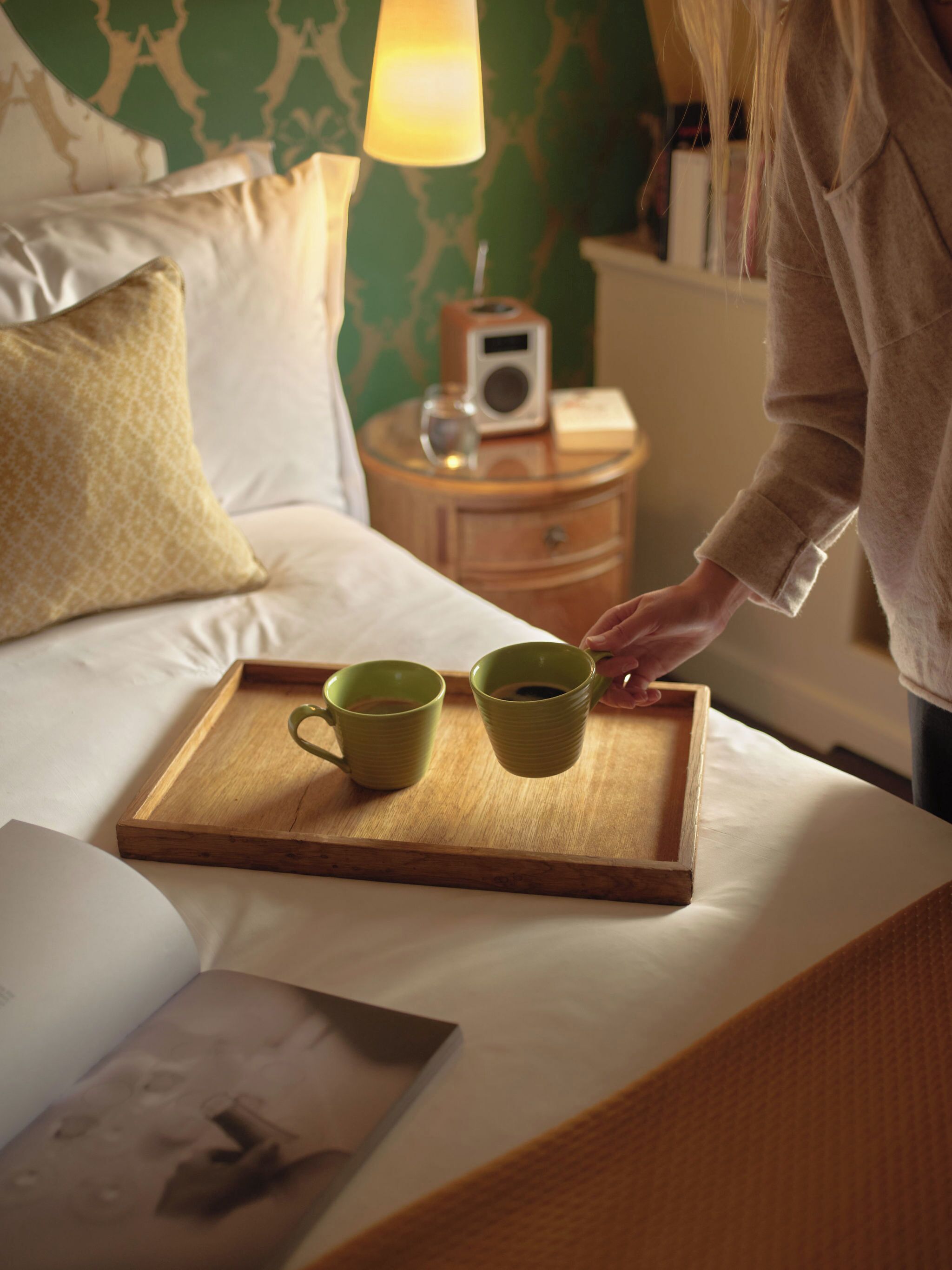 Una bandeja de madera con dos tazas verdes sobre una cama.