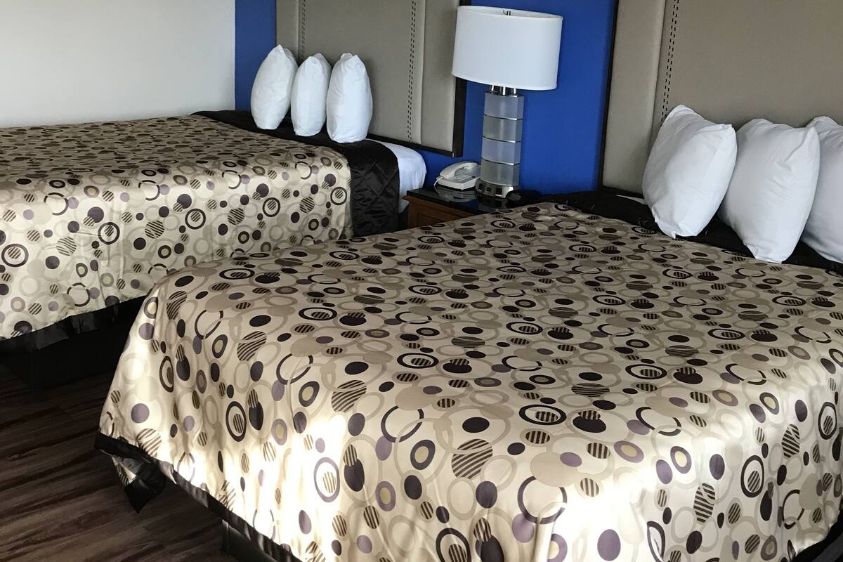 A hotel room with two beds, each with a headboard, a bedside table with a lamp, and a telephone.