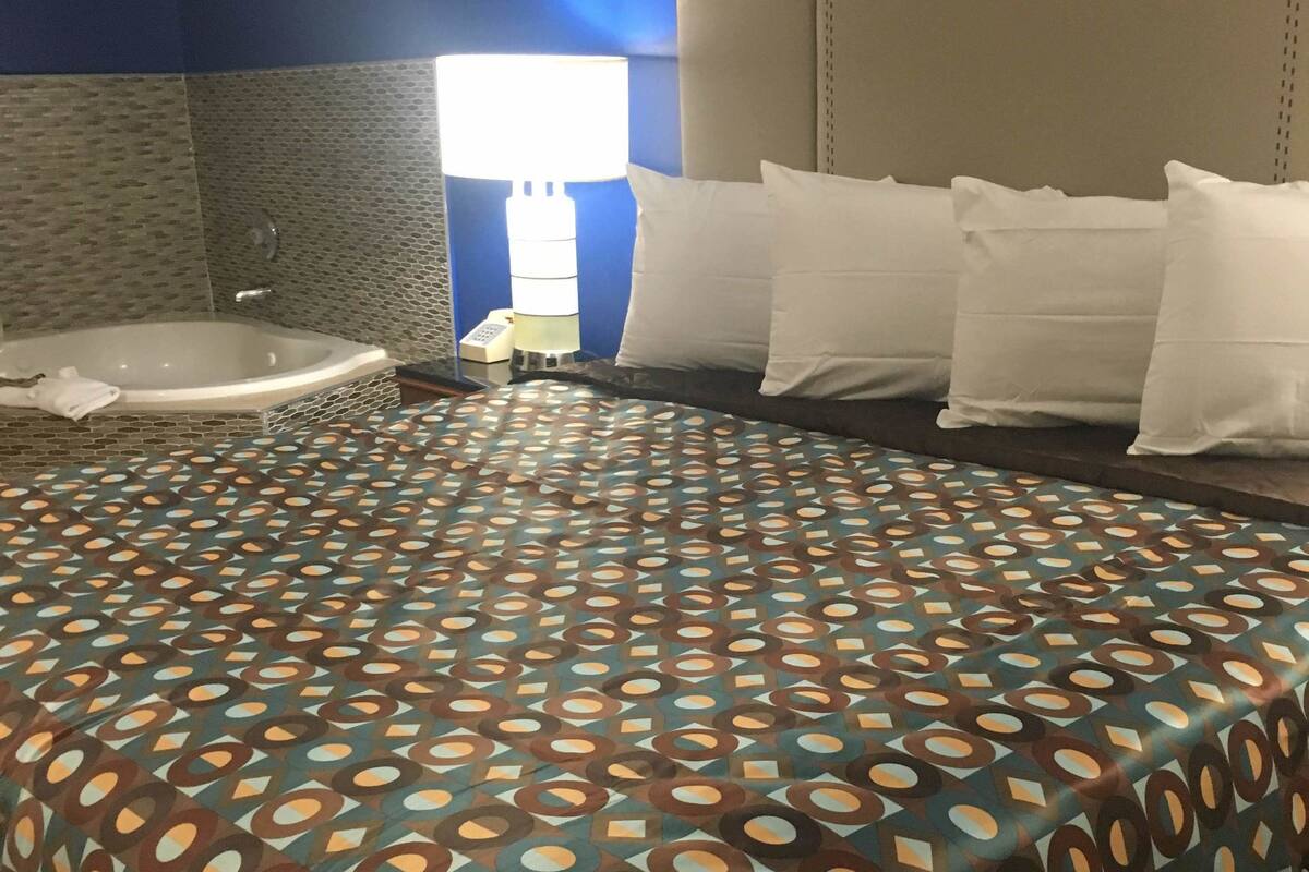 A hotel room with a large bed, a bathtub, and a nightstand with a lamp.