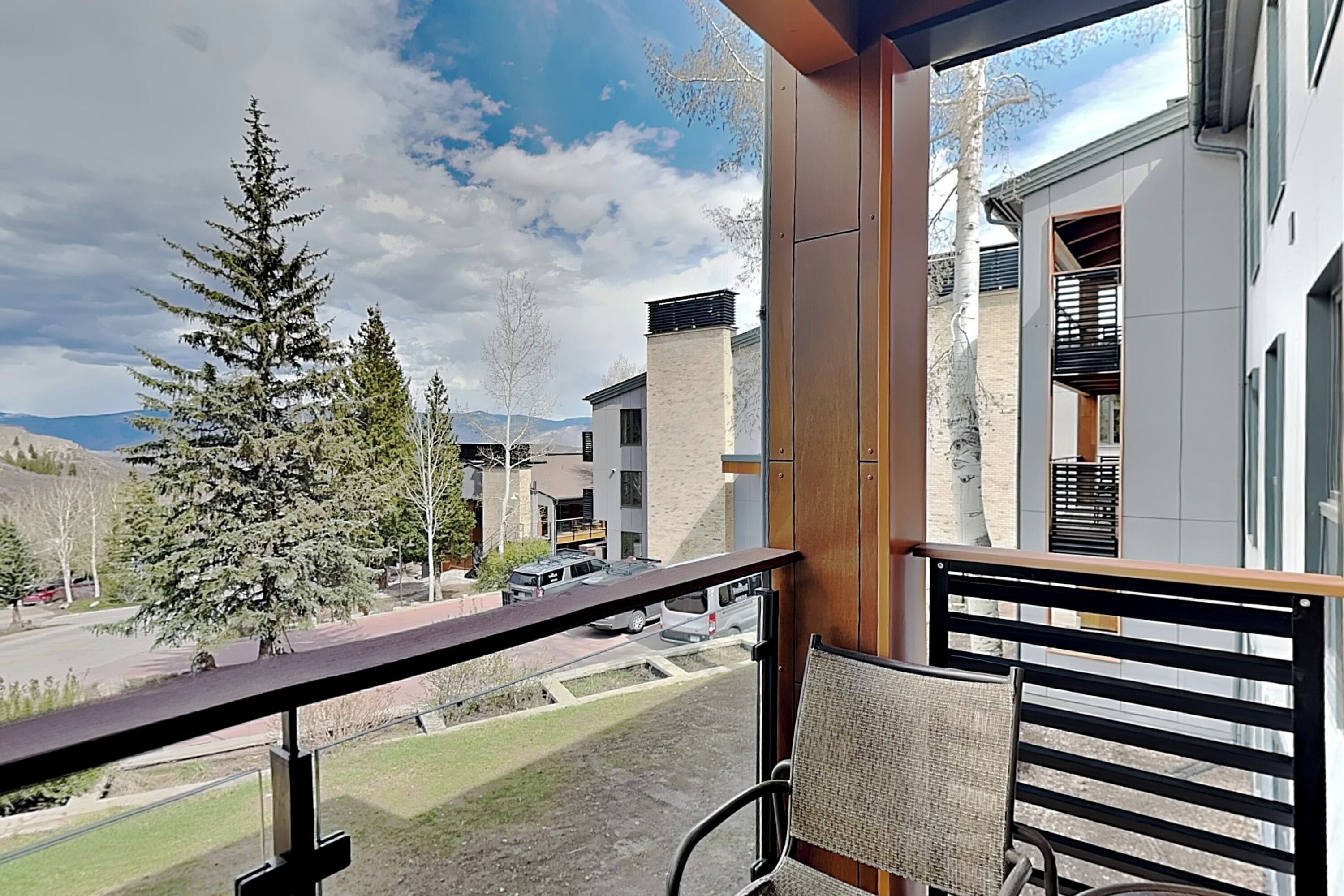 Un balcon donnant sur un immeuble moderne, un arbre et une route.