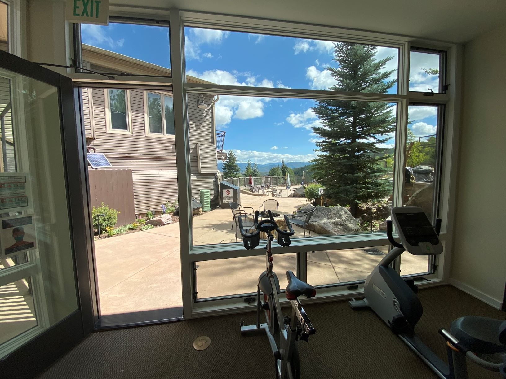 A gym with exercise equipment and a view of an outdoor area with a building and trees.