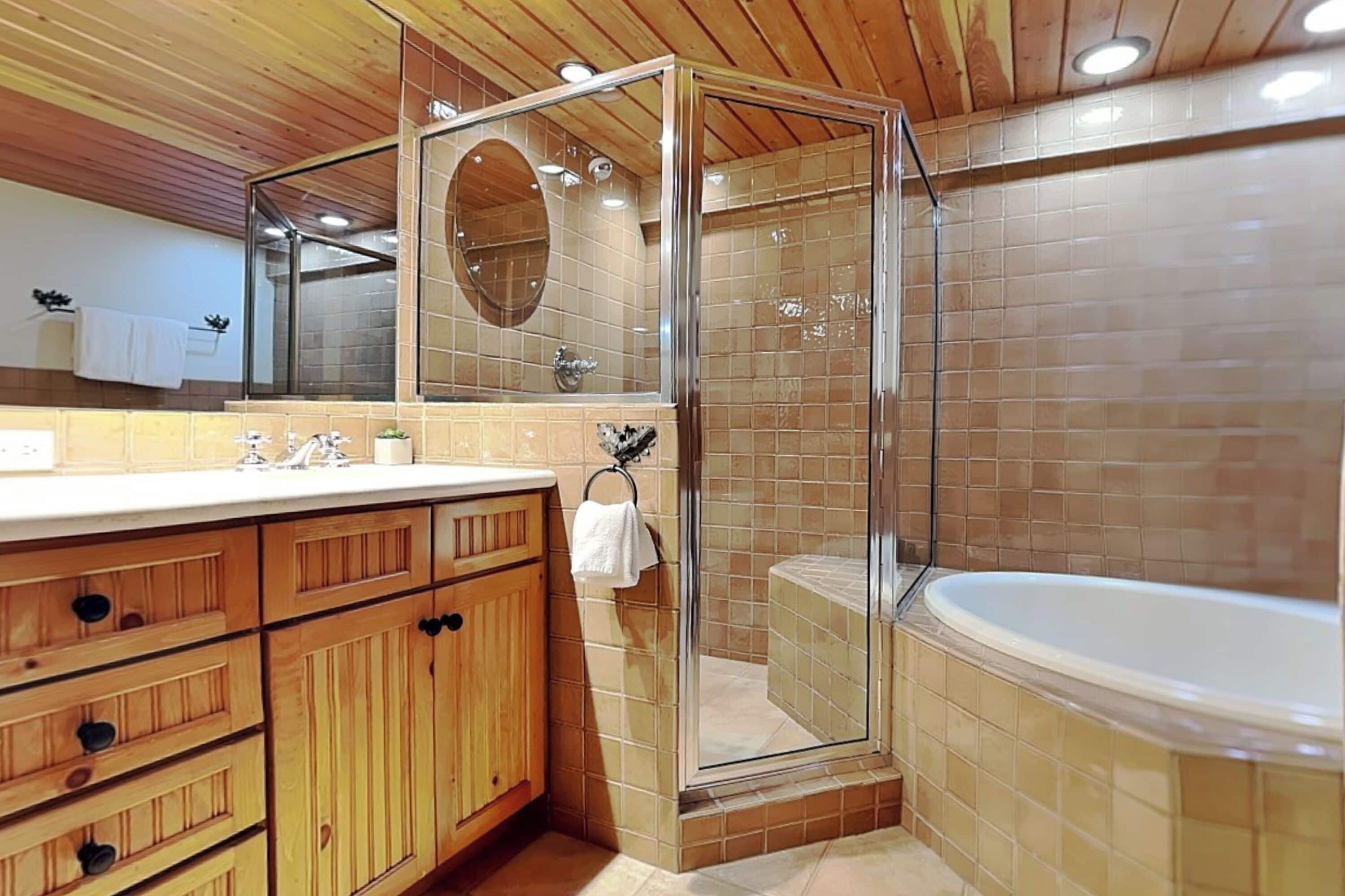 A modern bathroom with a glass-enclosed shower, a large bathtub, wooden cabinets, and a mirror.