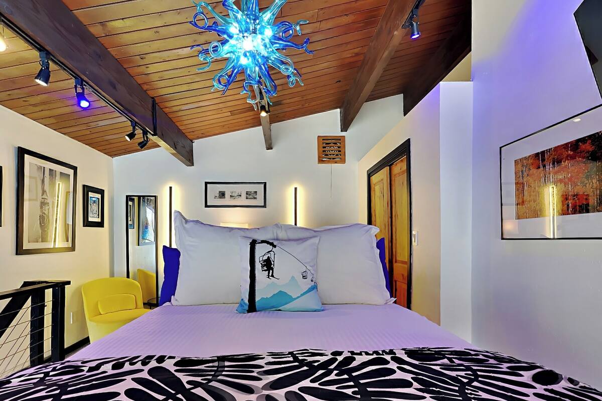 Une chambre à coucher avec un lit, un luminaire au plafond, des tableaux encadrés accrochés aux murs et un escalier.