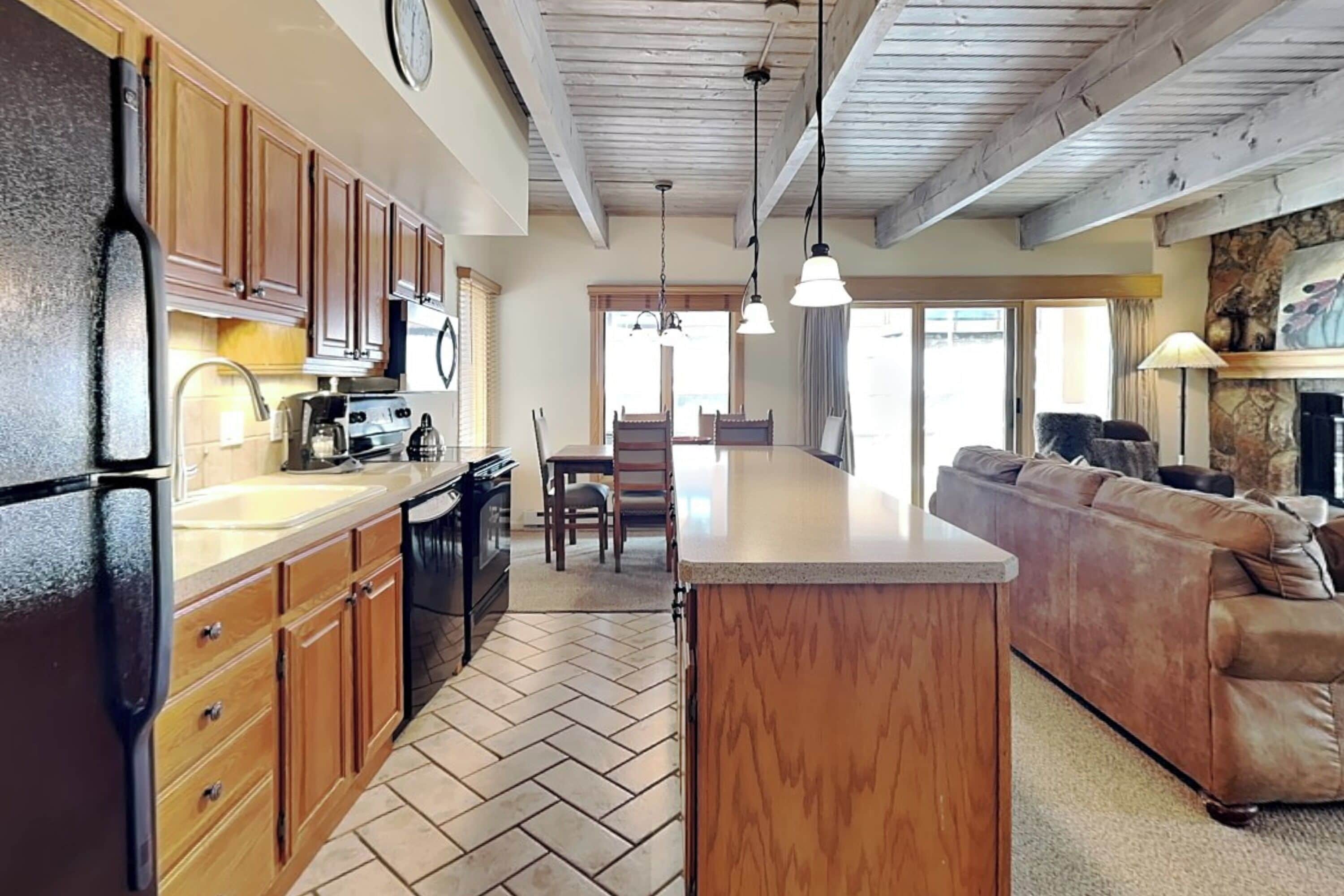 A kitchen with wooden cabinets, a refrigerator, a dining area with a table and chairs, and a living room with a sofa.