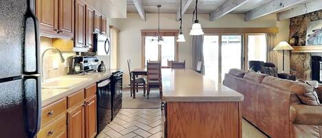 A kitchen with wooden cabinets, a refrigerator, a dining area with a table and chairs, and a living room with a sofa.