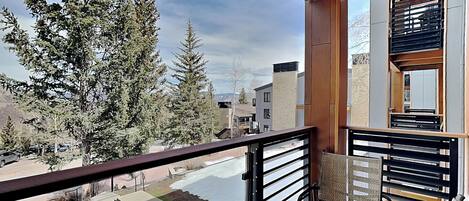 A balcony with a view of trees and buildings, a chair, and a railing.
