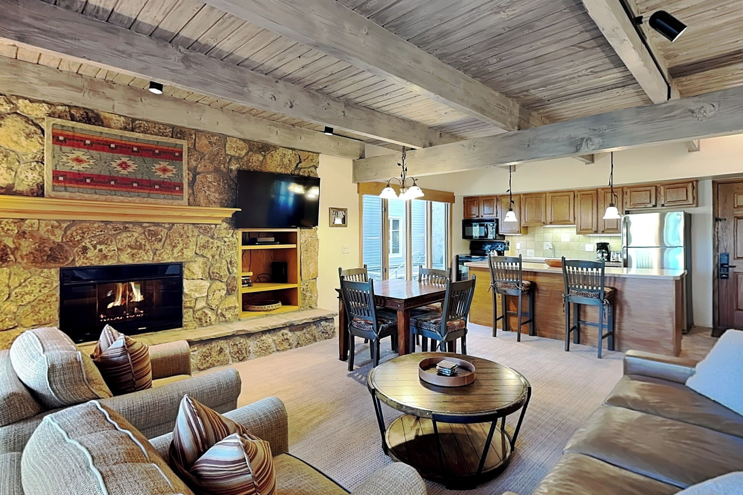 A spacious living room with a stone fireplace, a television, and a dining area with wooden chairs and a table.