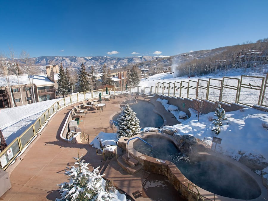 A snow-covered outdoor area with a hot tub, seating, and a view of mountains.
