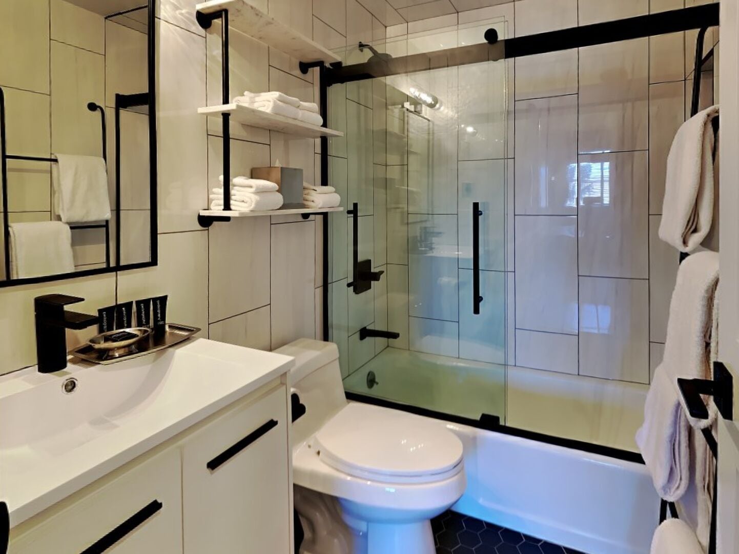 A modern bathroom with a glass-enclosed shower, white tiles, a white sink, and a toilet.