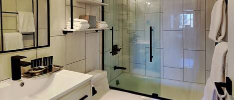 Un baño moderno con cabina de ducha de vidrio, azulejos blancos, lavamanos blanco y un inodoro.