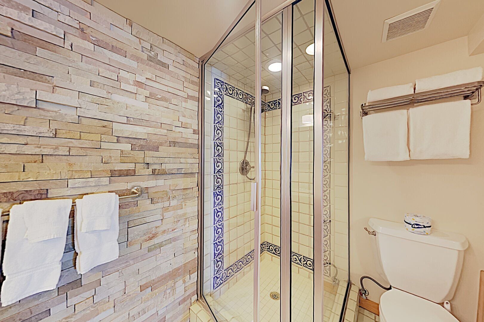 Une salle de bain avec un mur en pierre, une douche en verre et des toilettes dotées d’un porte-rouleau de papier toilette.
