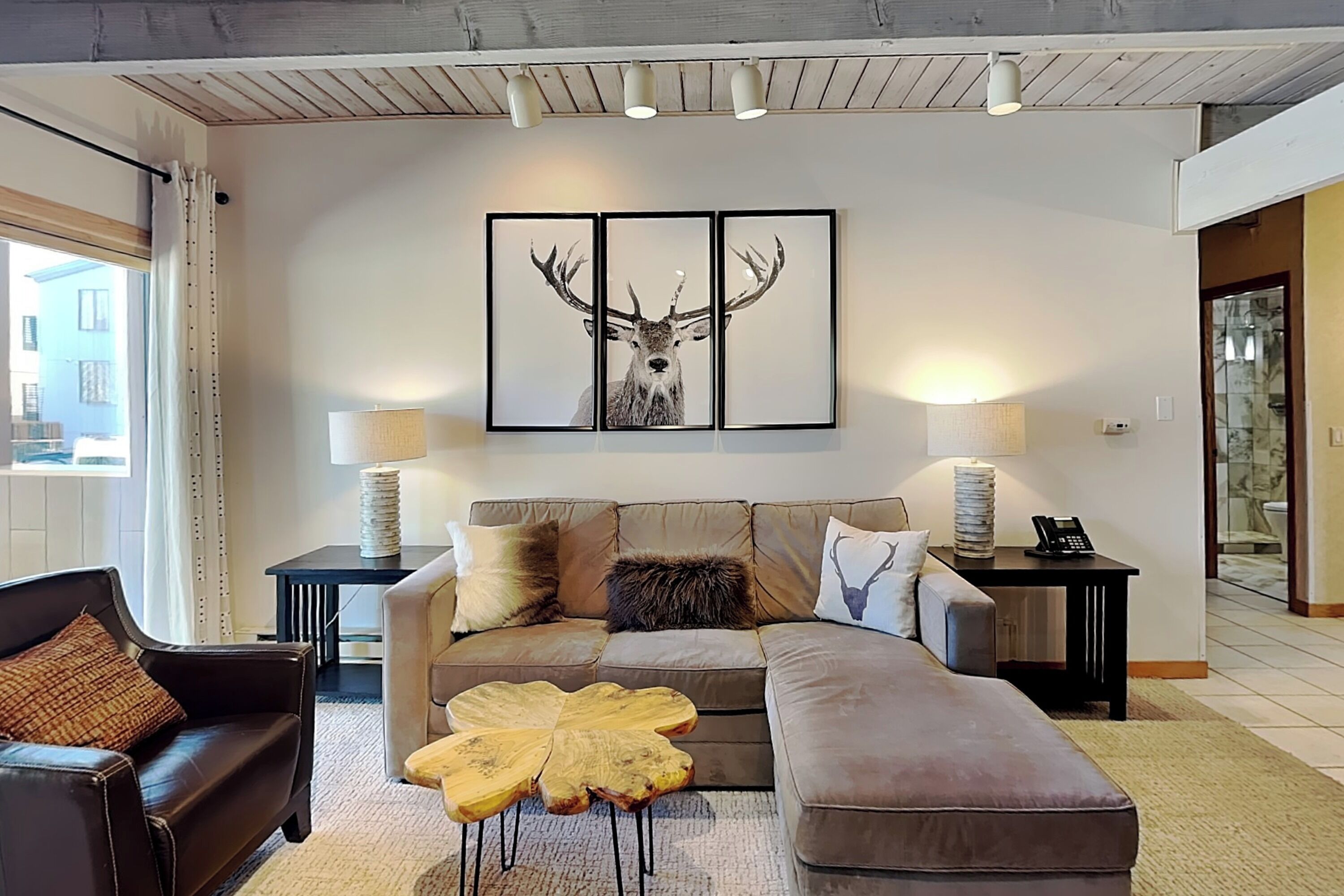 A modern living room with a large sofa, a coffee table, and a framed deer artwork on the wall.
