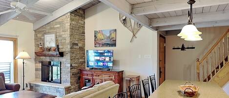Una sala de estar con chimenea de piedra, televisor y comedor con sillas y una mesa.