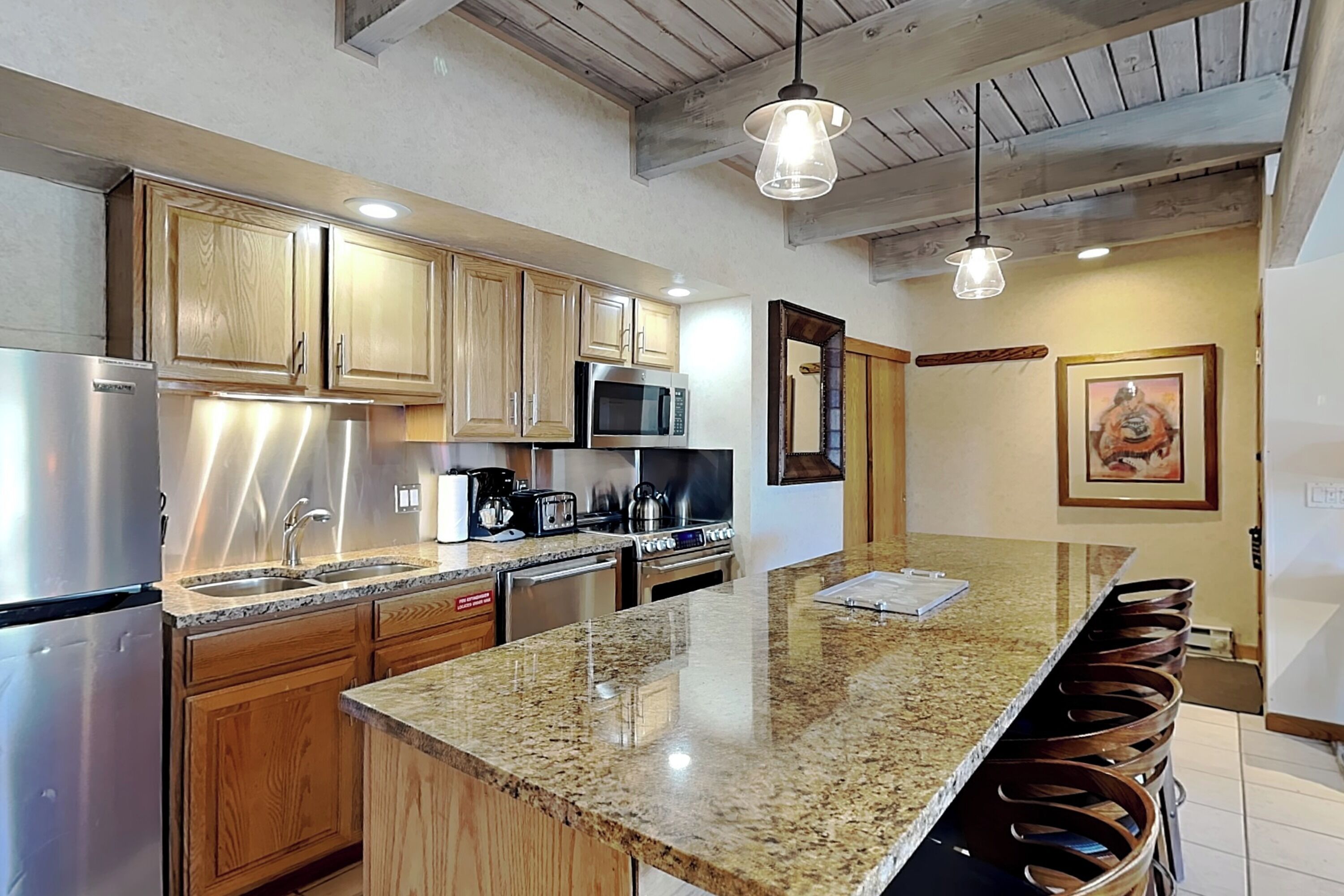 A kitchen with wooden cabinets, stainless steel appliances, granite countertops, and a bar area with stools.