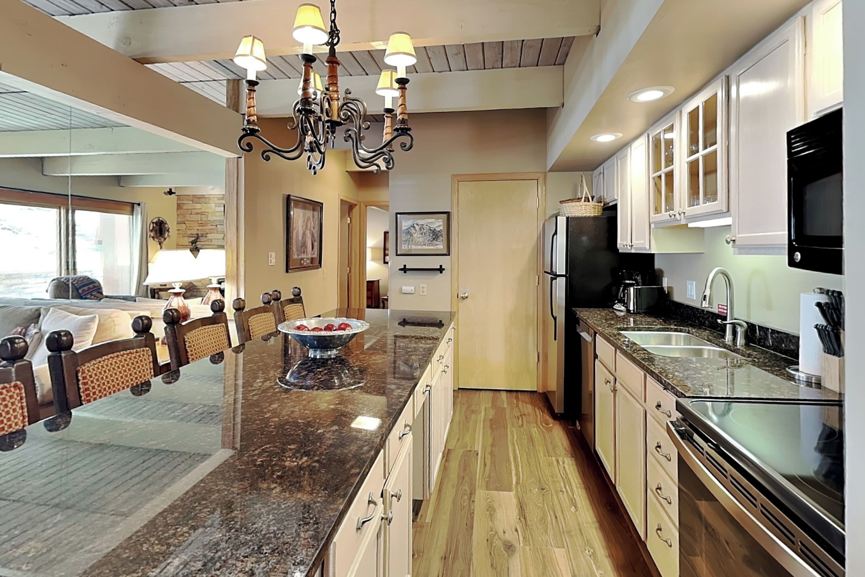 A modern kitchen with granite countertops, stainless steel appliances, and a chandelier.