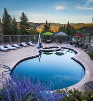 A swimming pool with lounge chairs and umbrellas, surrounded by a fence and overlooking a mountainous landscape.