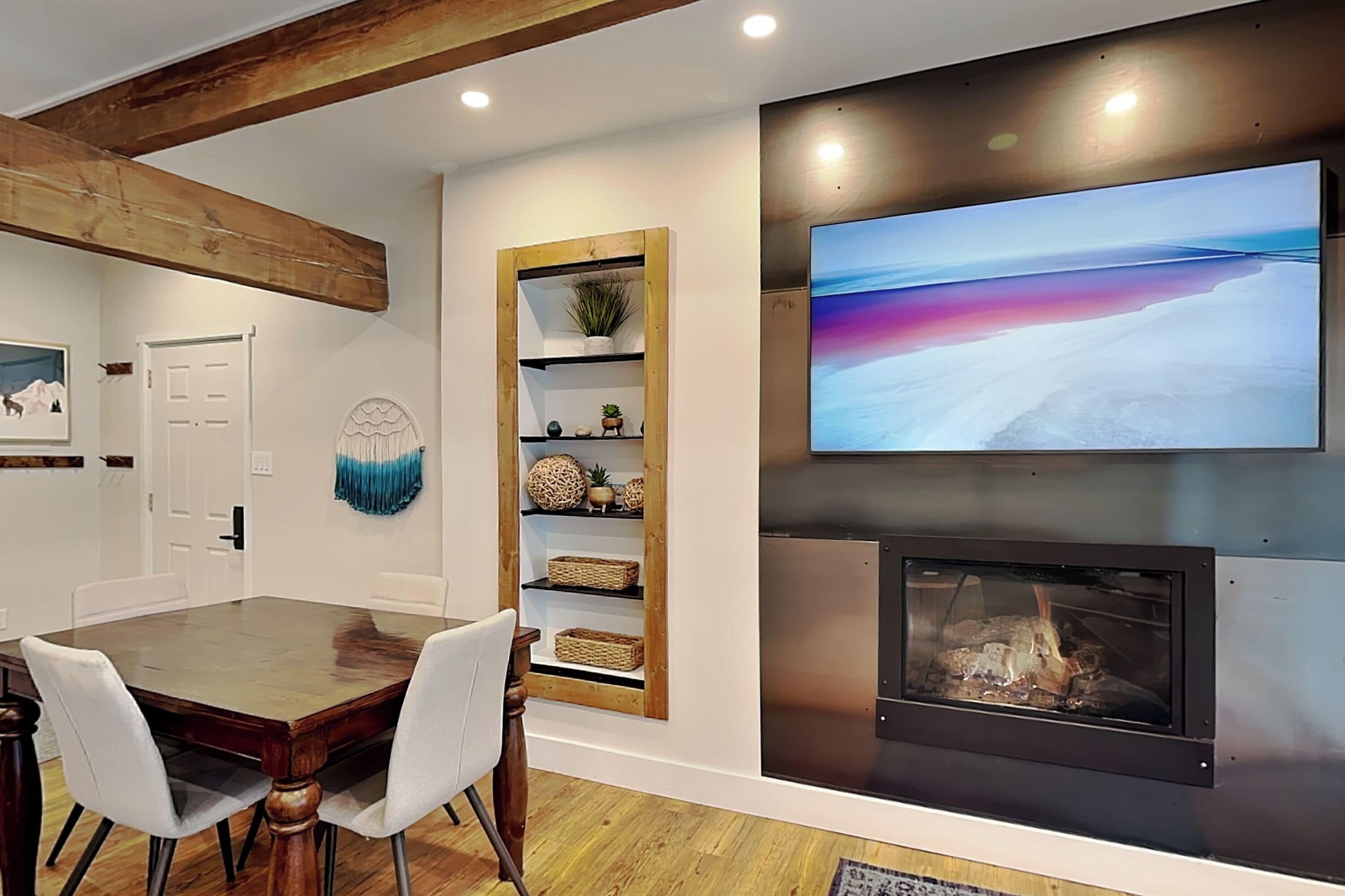 Un comedor con una mesa y sillas de madera, una chimenea, un televisor montado en la pared y un estante con objetos decorativos.