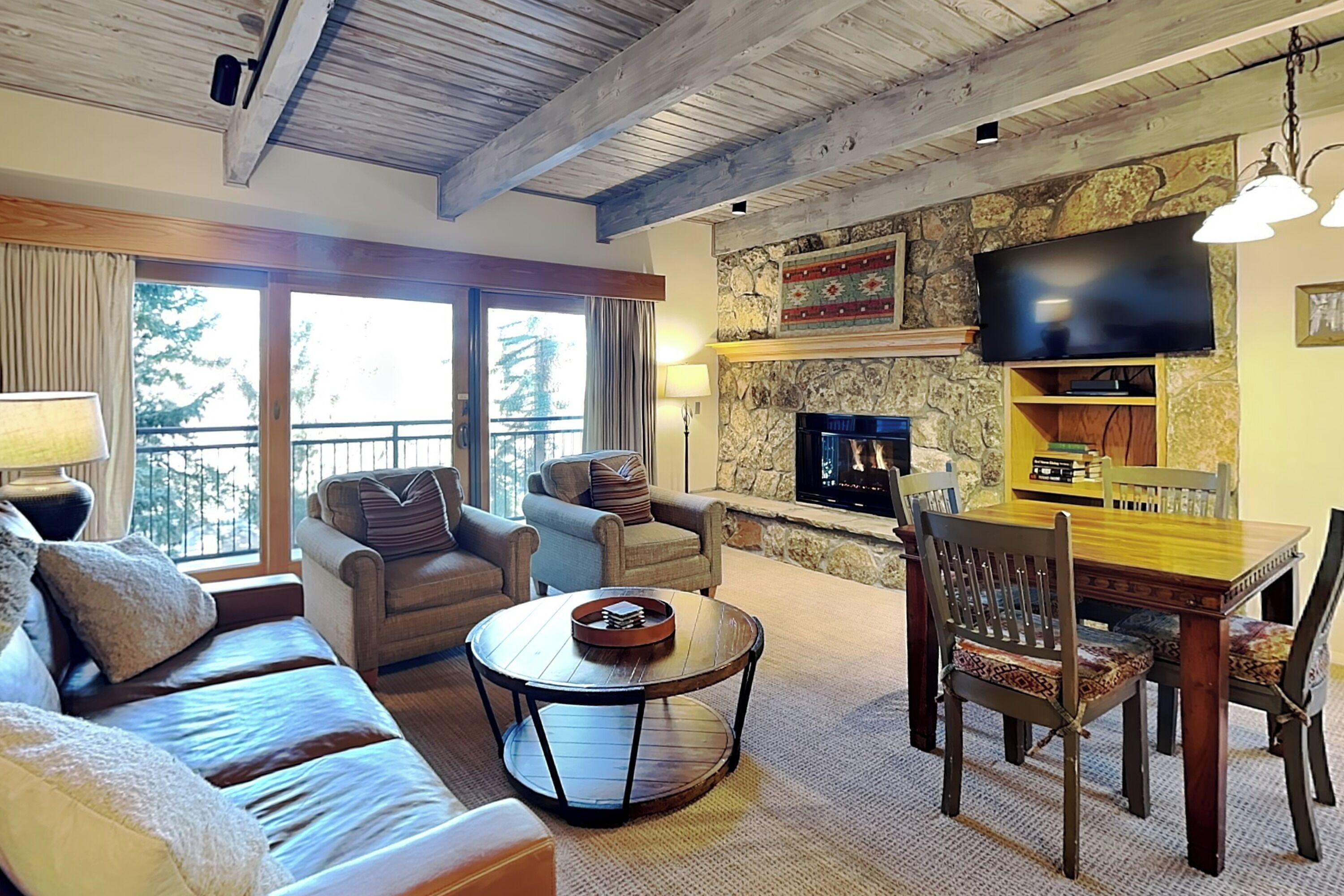A cozy living room with a stone fireplace, a flat-screen TV, and a dining area with wooden furniture.