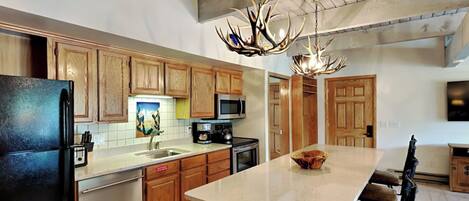 A kitchen with wooden cabinets, a black refrigerator, a microwave, and a large island with chairs.