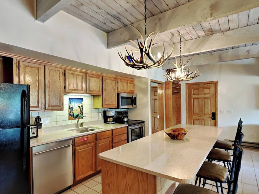 A kitchen with wooden cabinets, a black refrigerator, a microwave, and a large island with chairs.