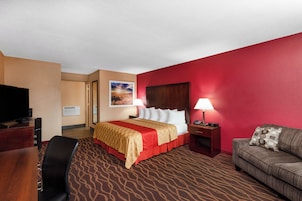 Quarto de hotel com uma cama, televisão, escrivaninha, cadeira, sofá e parede vermelha.
