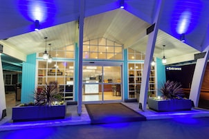 Entrada de hotel com porta de vidro, placa indicando a entrada e toldo azul.