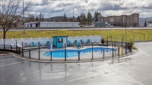 Una piscina con cubierta azul, rodeada por una cerca negra, y un pequeño edificio azul cerca.