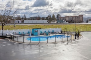 Piscina com deck azul, cercada por uma grade preta, e um pequeno edifício azul por perto.