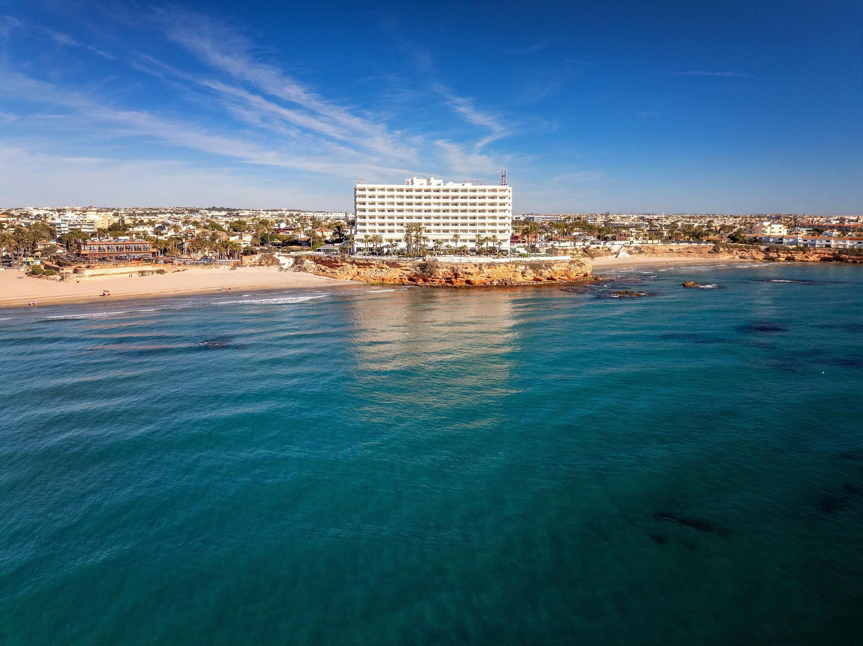 Un hotel frente al mar con un edificio grande y aguas azules cristalinas.