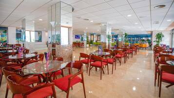 Um amplo saguão de hotel com várias áreas de refeições, mesas de vidro e cadeiras vermelhas.