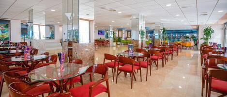 Un amplio vestíbulo de hotel con varias zonas de comedor, mesas de cristal y sillas rojas.